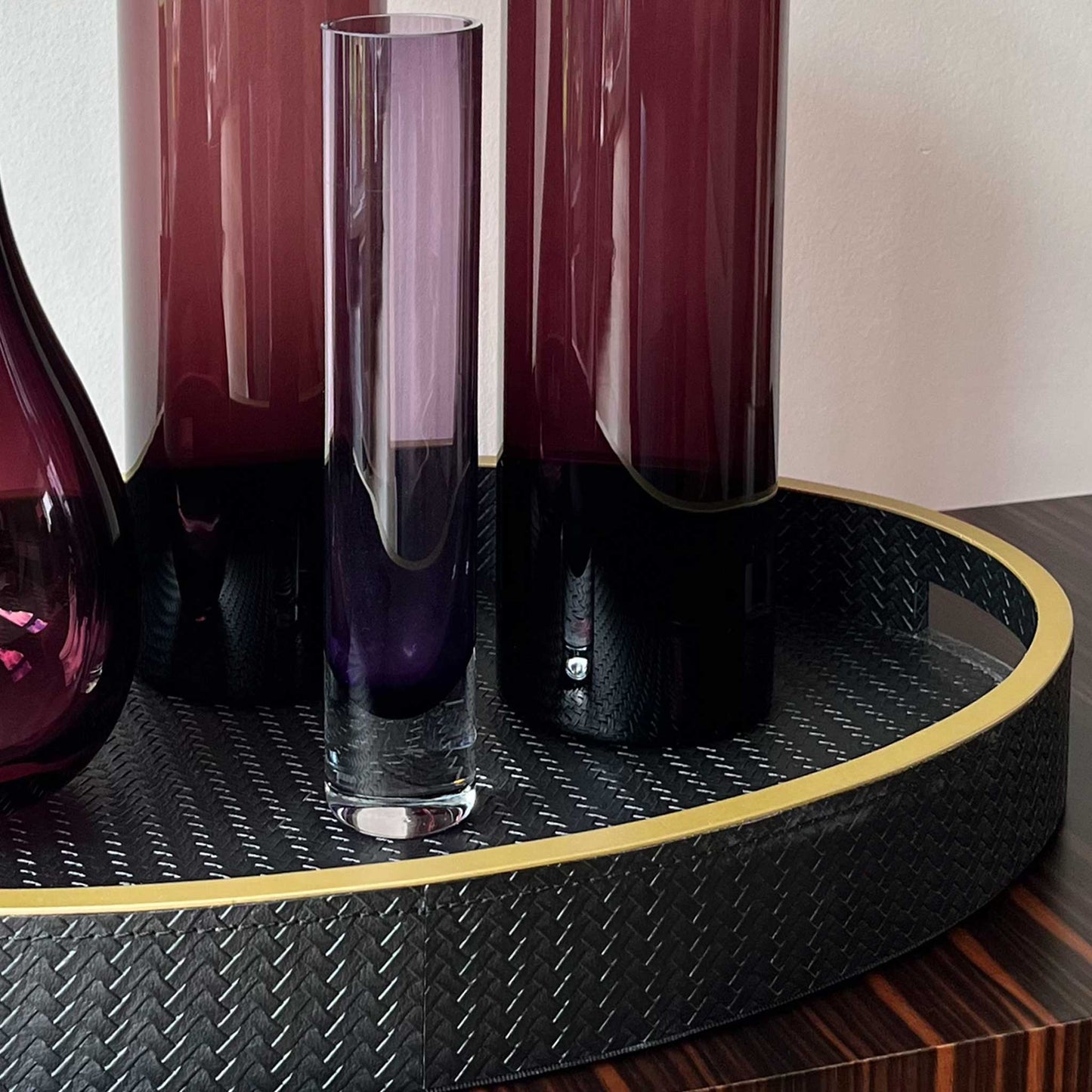 Close up of lifestyle image of oval black textured leather with gilt trim and handles. Displayed with purple vases.