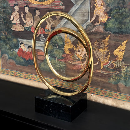 Lifestyle image of luxury round bronze decor Infinity Sculpture with marble block base, displayed against a Chinese tapestry