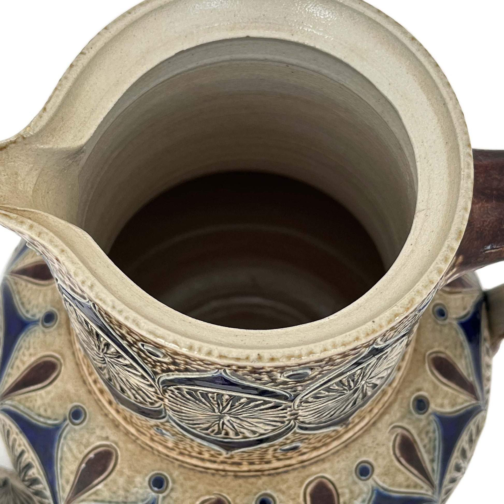 Close up of small coffee pot with decoration and engraved details in blue and brown seen from above with lid off.