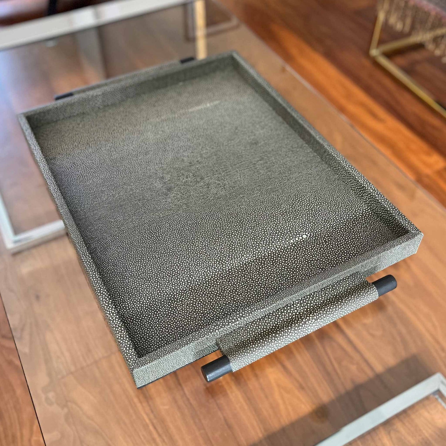 Lifestyle image of embossed grey shagreen textured leather, with wooden handles finished in carbon and leather wrapped. Shown on modern glass and chrome table with expensive wooden floor.