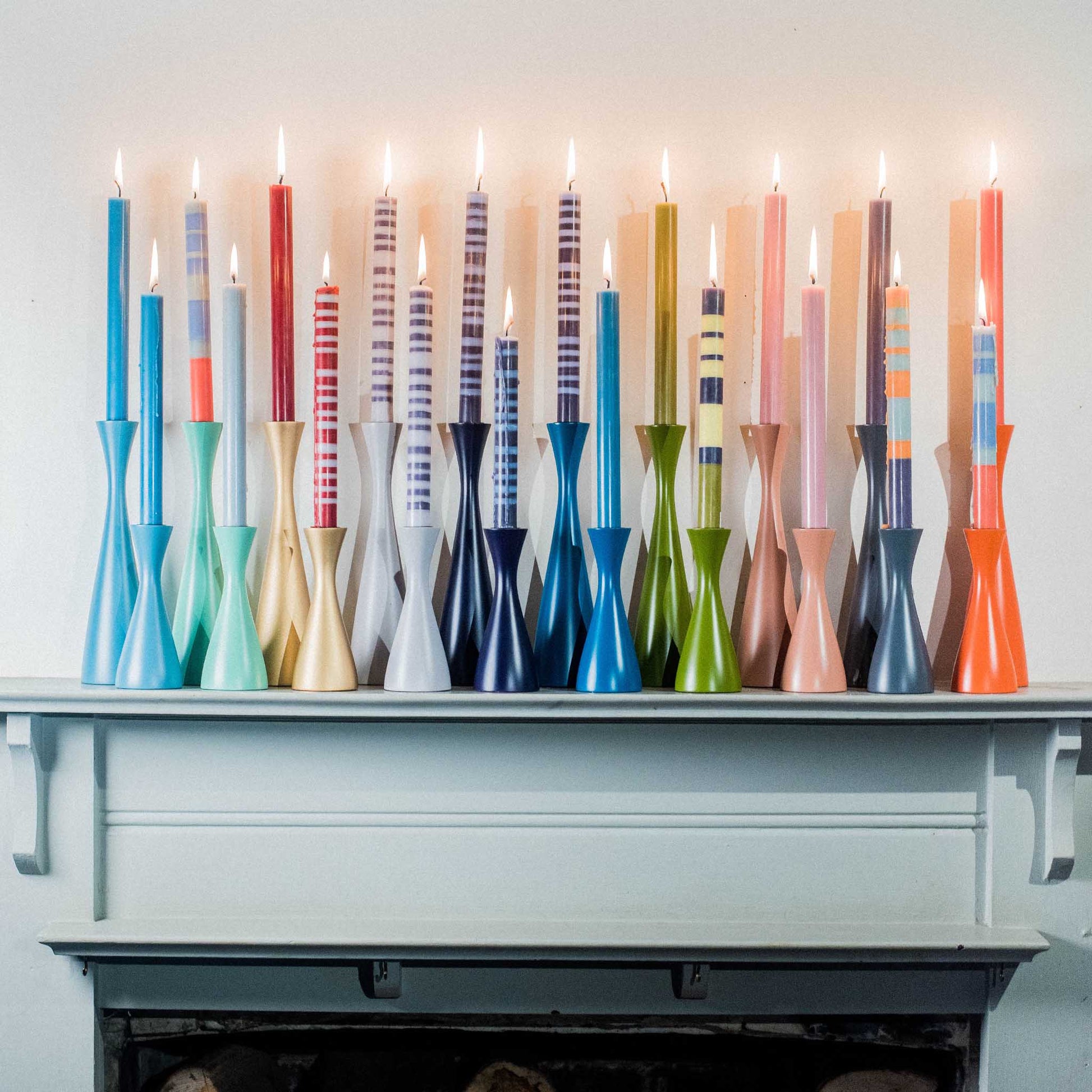 lifestyle shot of the striped candle collection in matching candle holders, on a fireplace mantlepiece