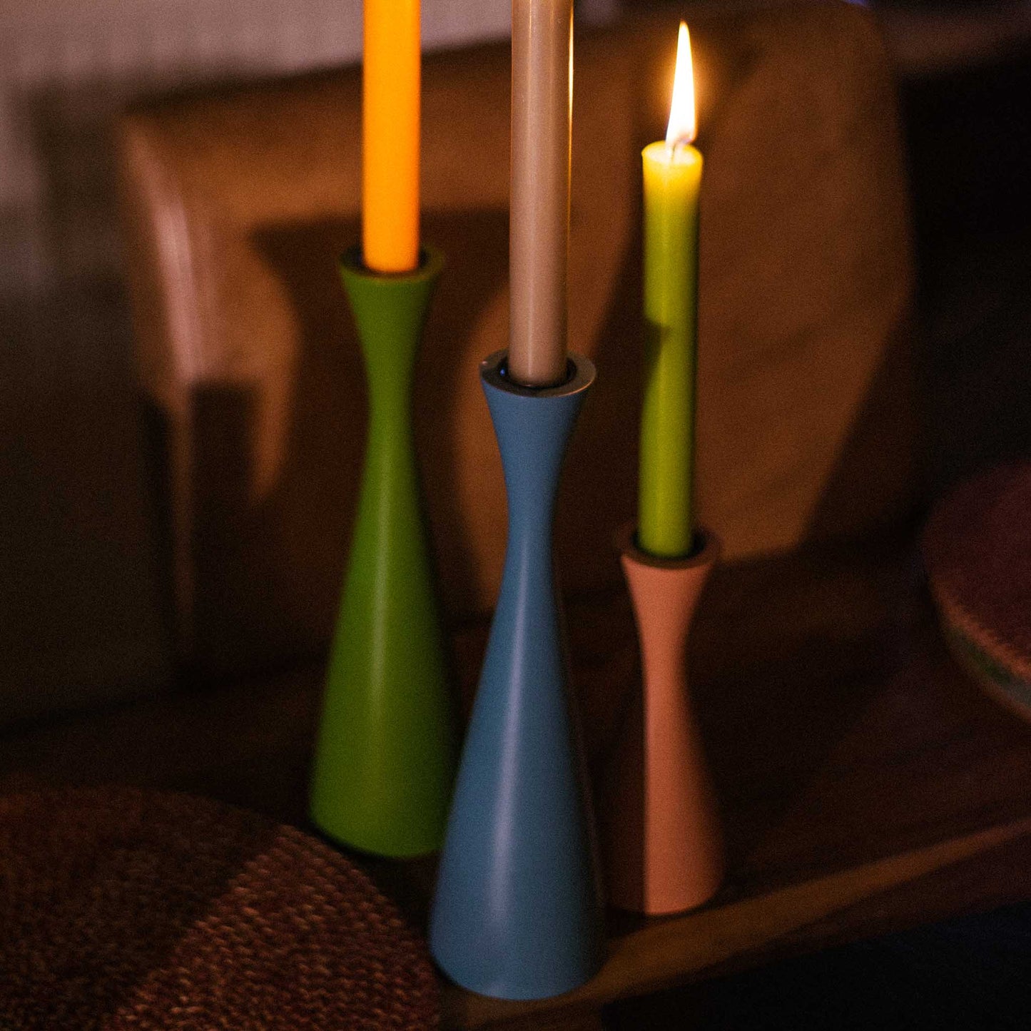 Close up of lifestyle image of three minimal green, blue and rose pink candleholders. Displayed on a table setting with romantic candlelight.