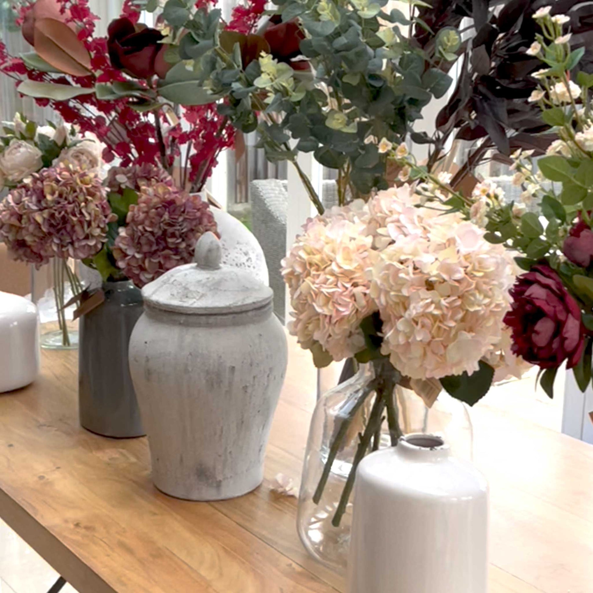 Lifestyle image of variety of vases, faux flowers and rustic ginger jar