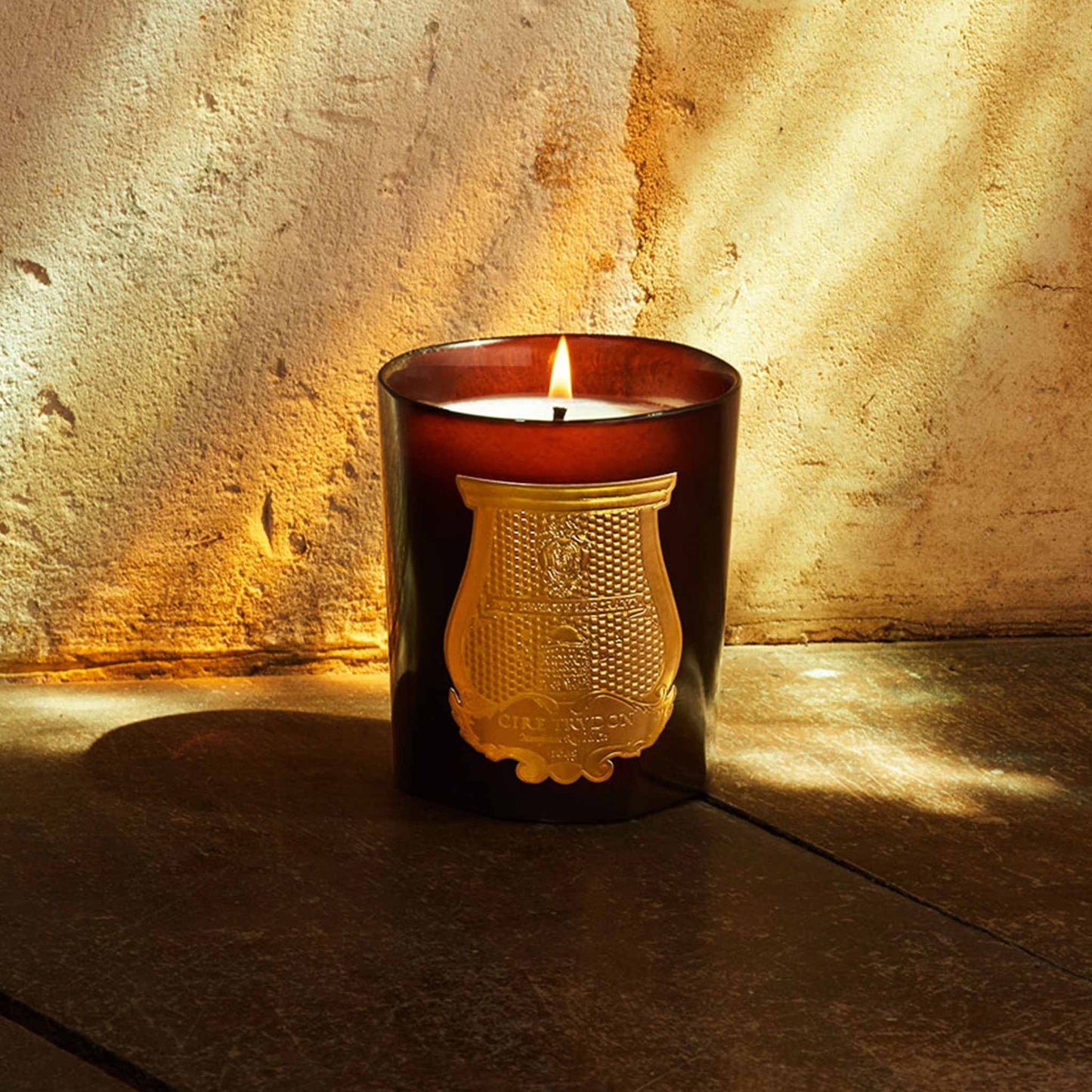 lifestyle image of a lit red jar cire trudon candle with a luxury gold label