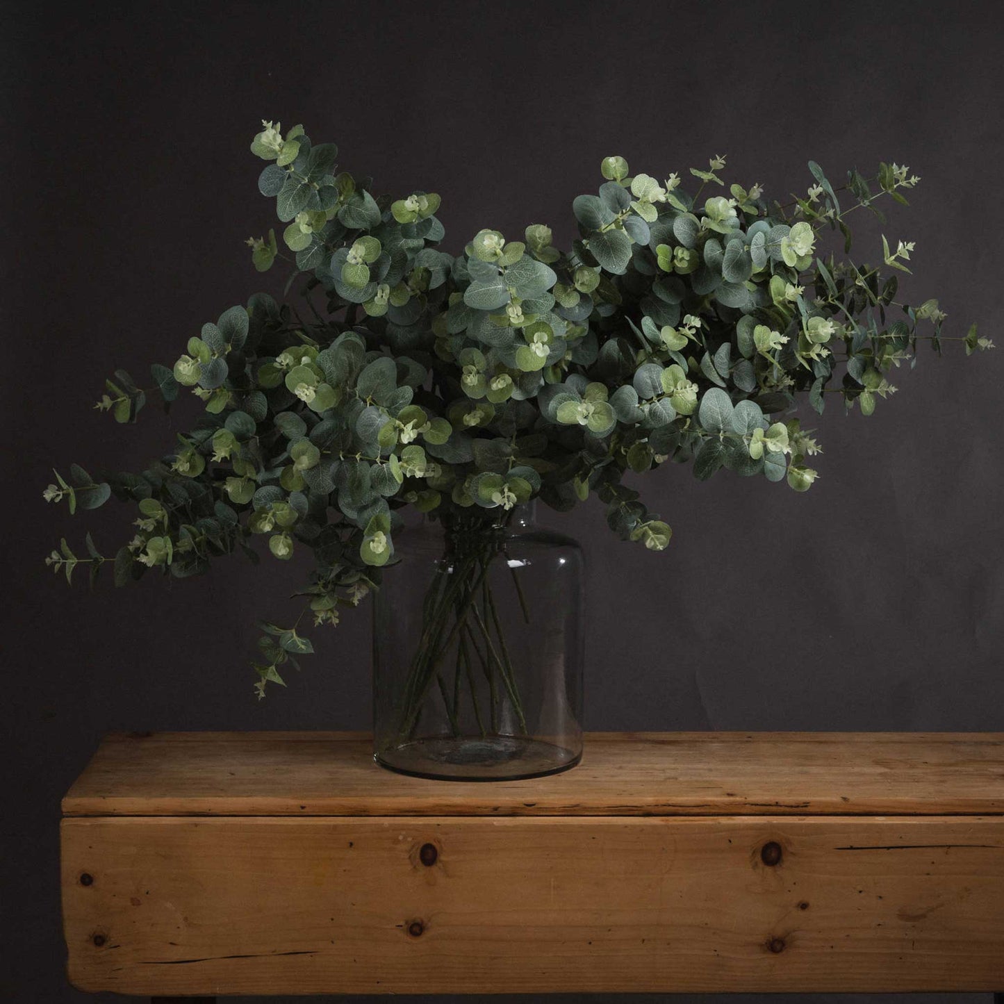 Lifestyle image of bunch of faux eucalyptus stems in rustic setting 