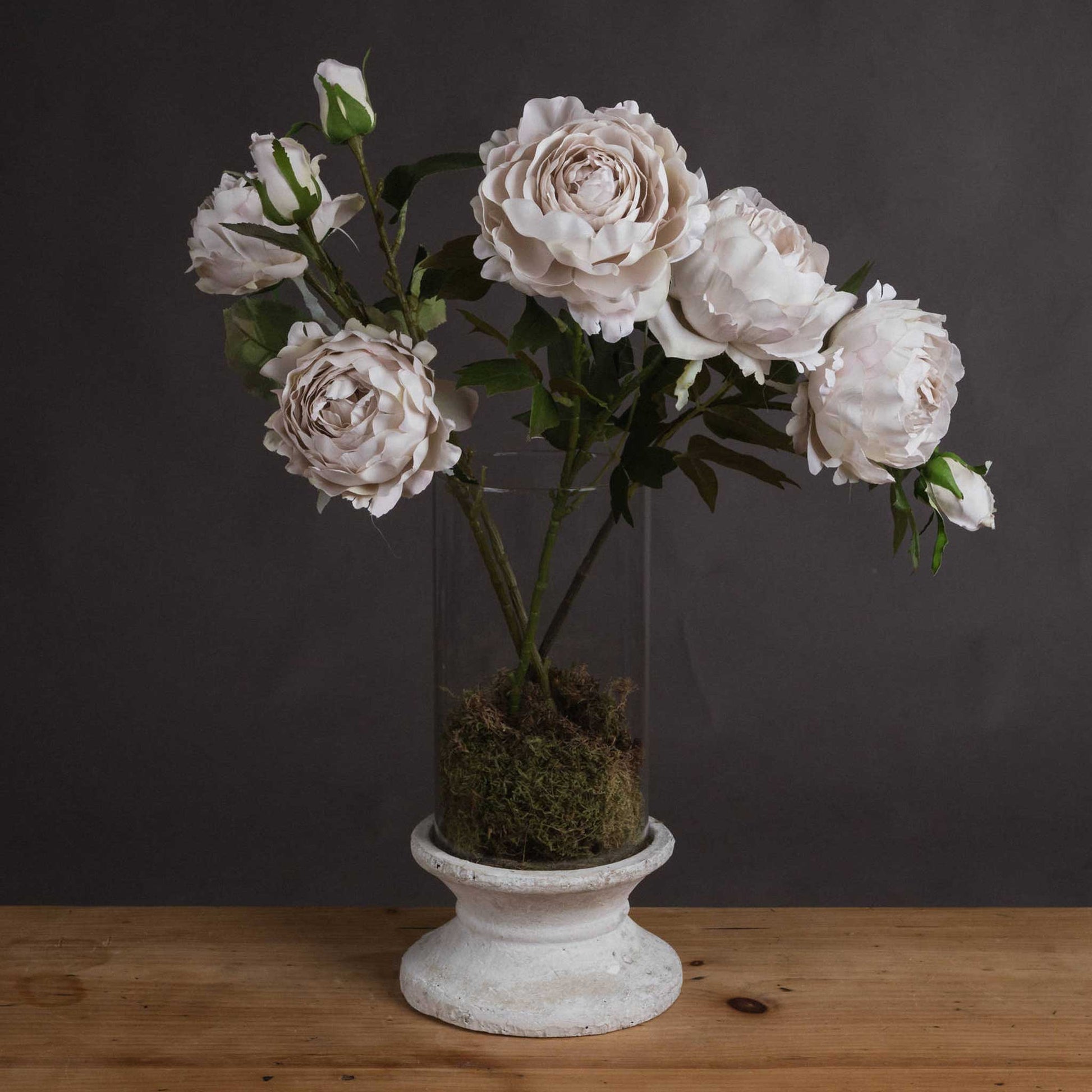 Lifestyle image of bunch of faux grey peony roses in a glass vase with moss.