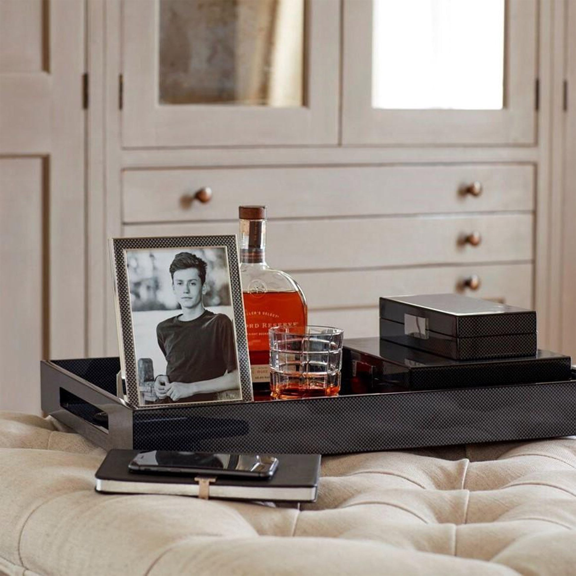 Lifestyle image of Carbon Fibre Lacquer Box, tray and frame. Displayed on ottoman in luxury living room.