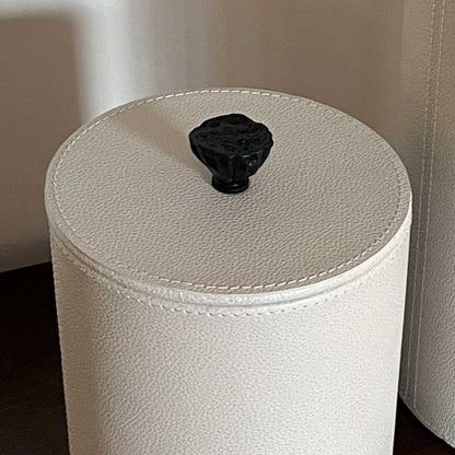 Close up lifestyle image of light cream leather cylinder box with cast brass handle 