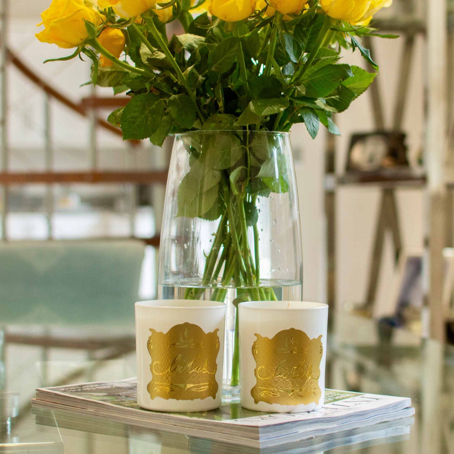 Lifestyle image of two Ludus candles displayed with a bunch of yellow roses.