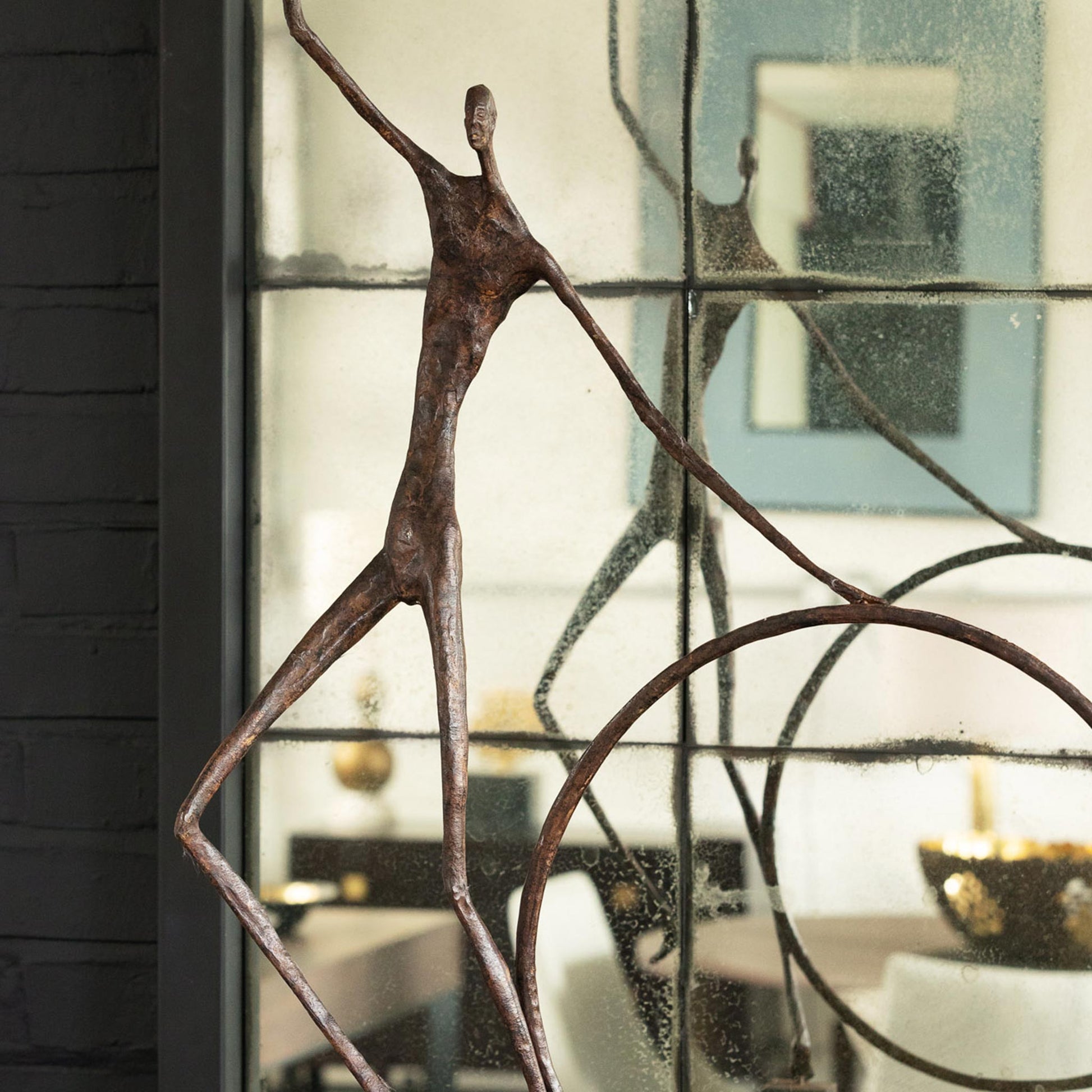 Close up of luxury bronze Giacometti style figure with hoop and stick. Displayed on a square bronze base, shown with reflection in mirror behind.