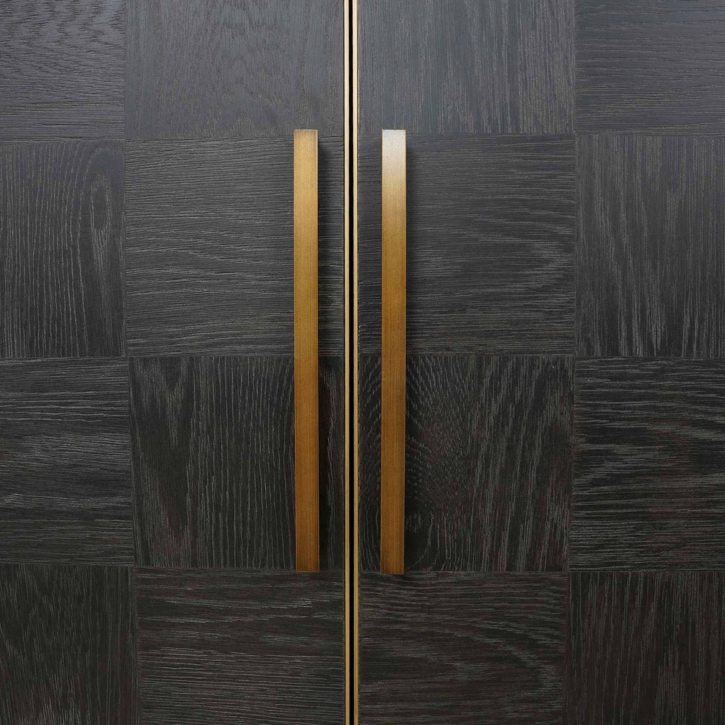 Close up of dark oak four door cabinet with long brass handles and brass feet