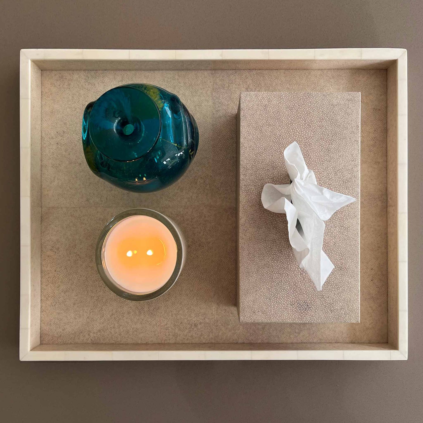 Lifestyle image of rectangular natural shagreen luxury tissue box displayed on a matching shagreen tray with a lit candle