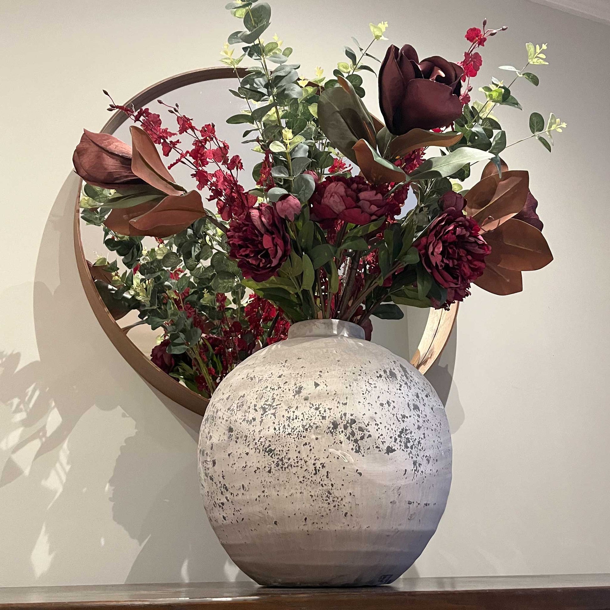 Lifestyle image of large rustic and stone effect spherical ceramic vase with faux flowers. 