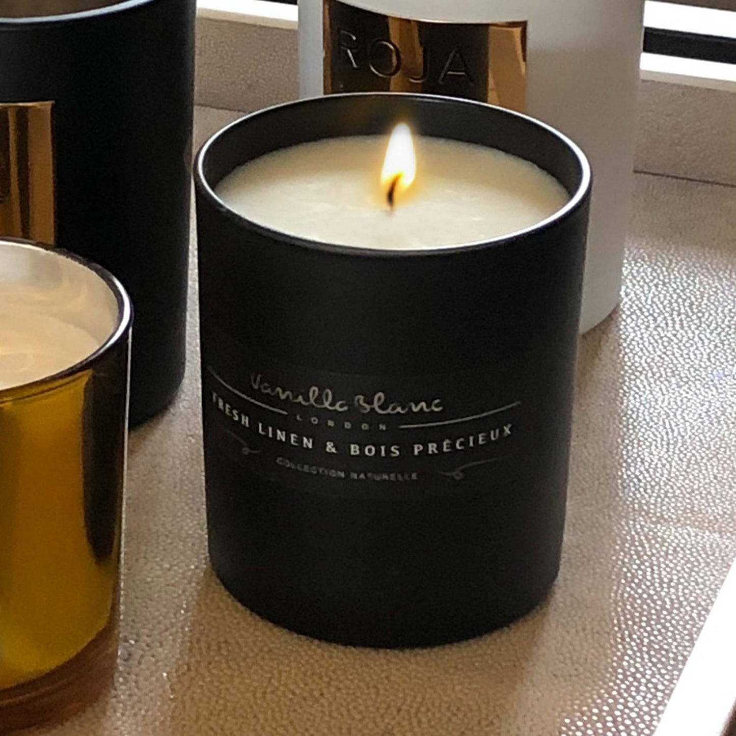 Lifestyle image of fresh Linen and Boix Précieux organic candle in matt glass jar. Collection of candles displayed on a decorative shagreen tray.