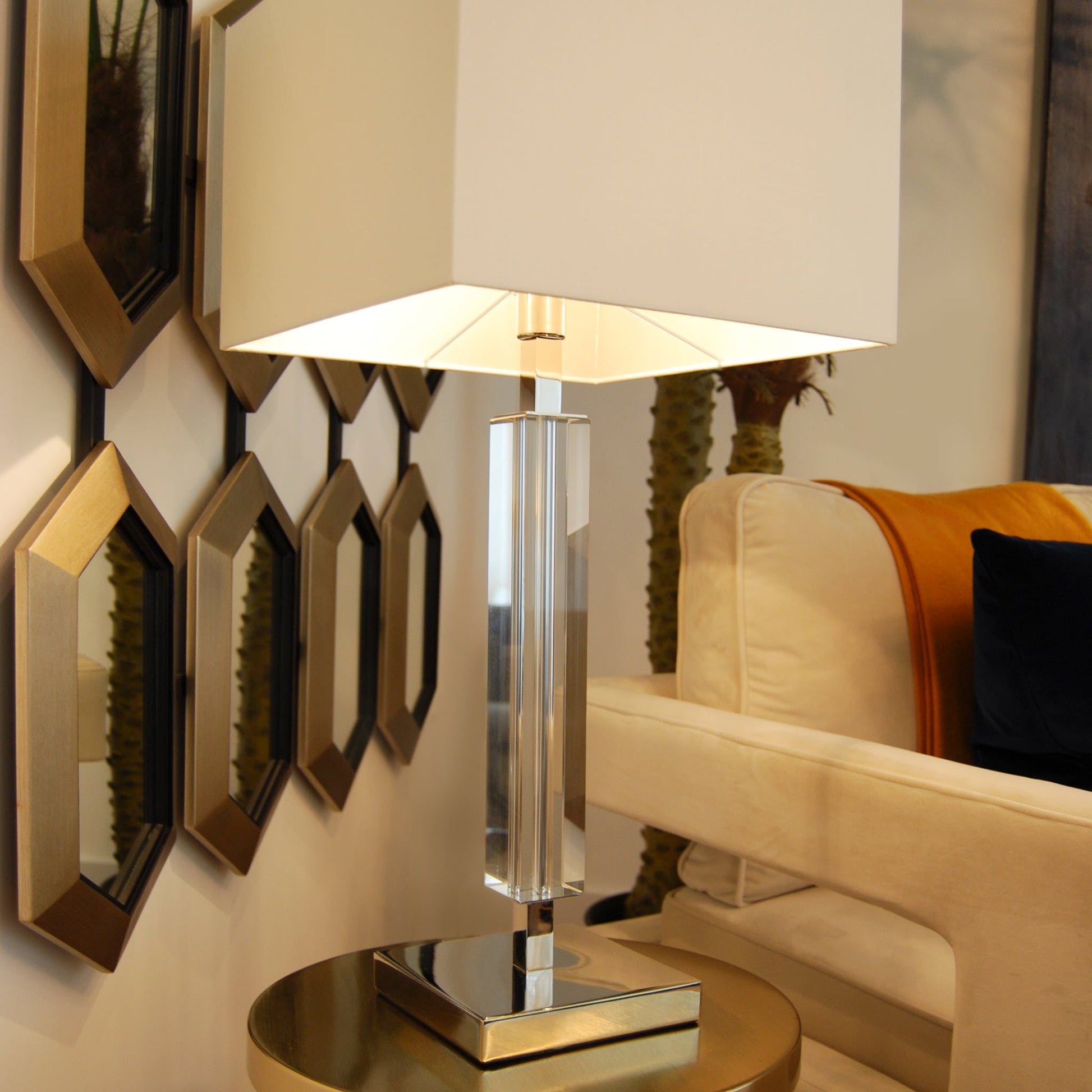 a lifestyle image of a modern sleek crystal table lamp, with rectangular white shade  on a side table in a luxury home